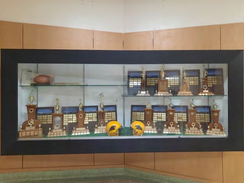 The Black Kats trophy case: wooden award trophies with engraved plaques and two gold helmets