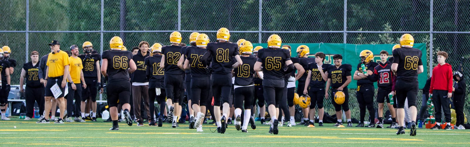 The Black Kats team on the field before a game, in black jerseys and yellow helmets